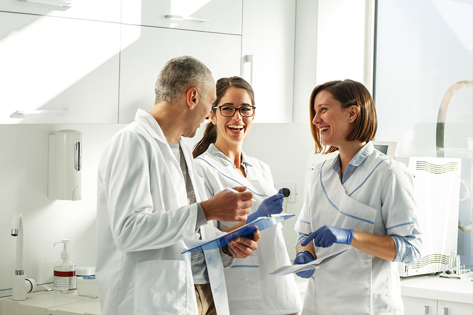 Three people in white lab coats standing in a laboratory, engaged in conversation while surrounded by scientific equipment.
