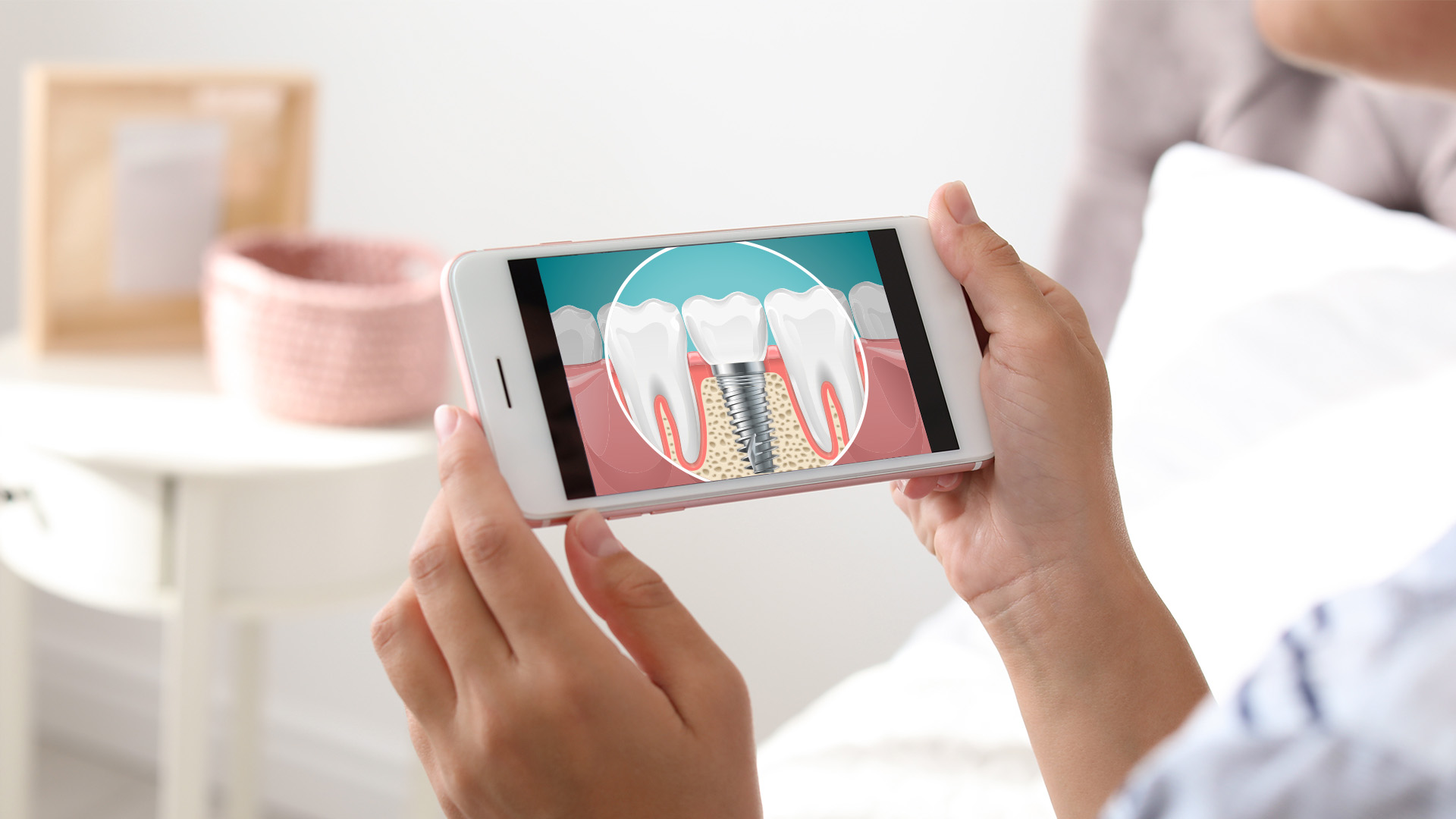 The image shows a person holding a smartphone displaying an illustration of teeth with dental implants, indicating the use of technology to visualize dental care options.
