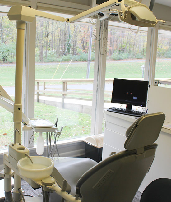 The image shows a dental chair setup with various equipment, including a computer monitor and a dental light, in an office that appears to be a dental practice.