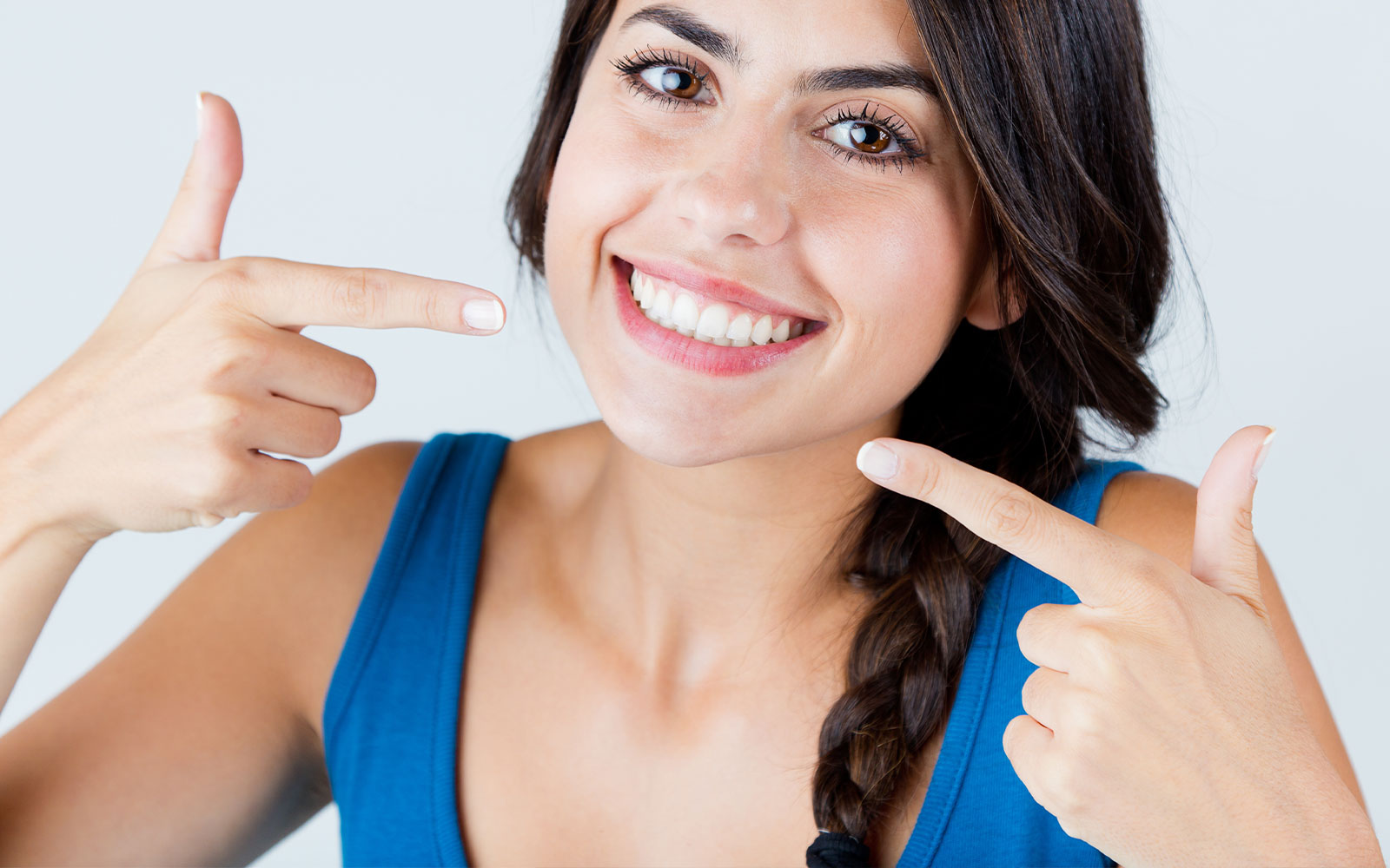 Smiling woman pointing at her teeth with both hands, showcasing a dental product or service.