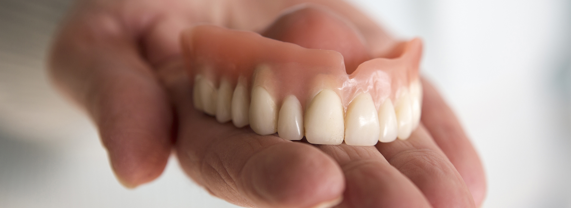 An individual holding a set of dentures, showcasing the upper and lower teeth.