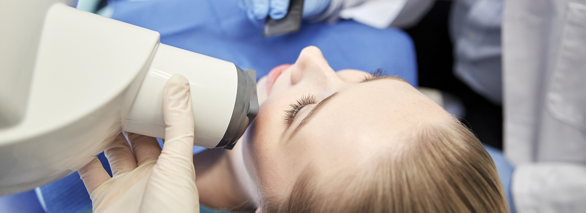 An individual receiving a dental implant procedure, with a dentist operating the equipment and a surgical setting visible in the background.