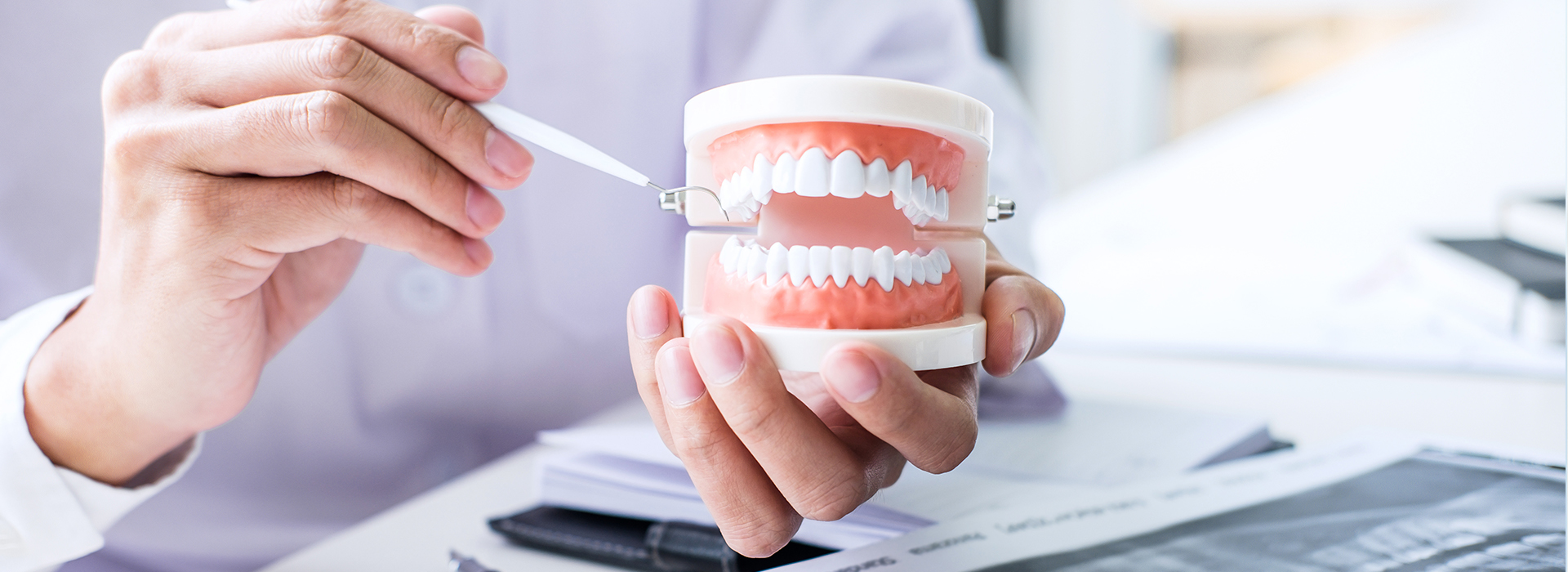 A person is holding a toothbrush with a toothpaste tube, while another person, possibly a dentist, is examining their teeth in a dental office setting.